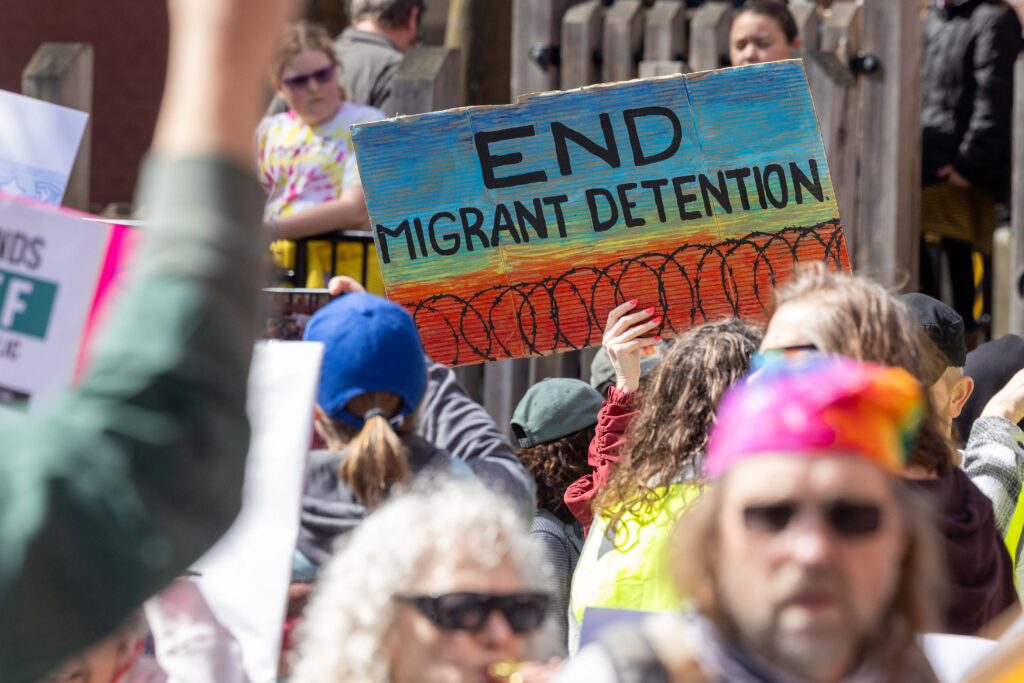 A protester holds a sign that reads "End Migrant Detention"