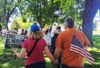 Two protesters, a woman and a man, face away from the camera. The woman, left, carries a sign that reads "This is not normal" and "No kings in America". The man, right, has a small American flag in his back pocket.